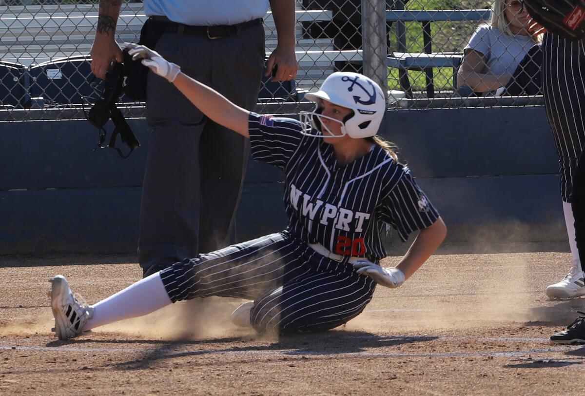 Newport Harbor's Ella Munzell slides safe at home against Corona del Mar in the Battle of the Bay softball game.
