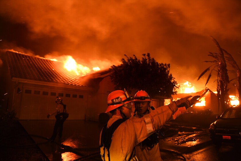 Deux pompiers parlent alors que les flammes dévorent les maisons derrière eux.