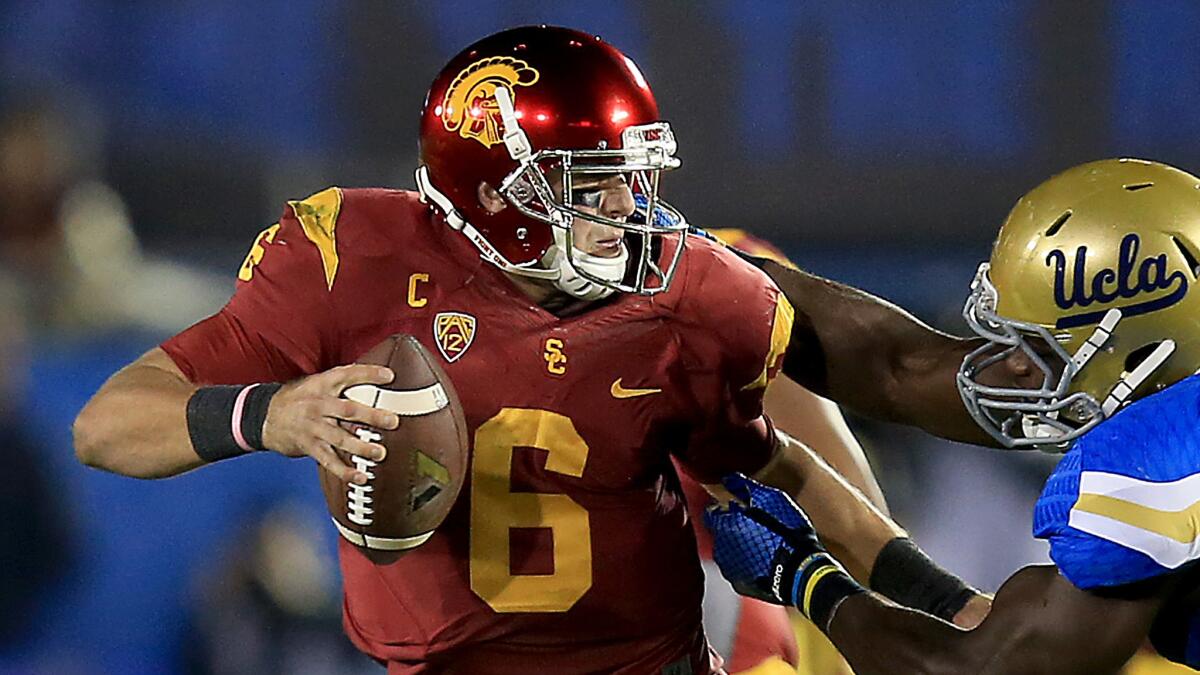USC quarterback Cody Kessler, left, tries to avoid being sacked by UCLA defensive lineman Owamagbe Odighizuwa during a game at the Rose Bowl on Nov. 22, 2014.