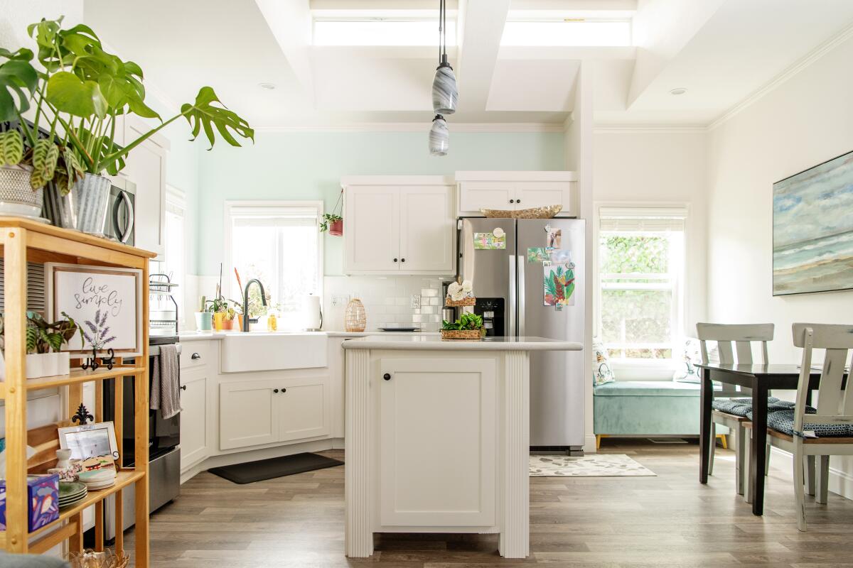 A white island sits in the middle of a kitchen bookended by cabinetry and a kitchen table.