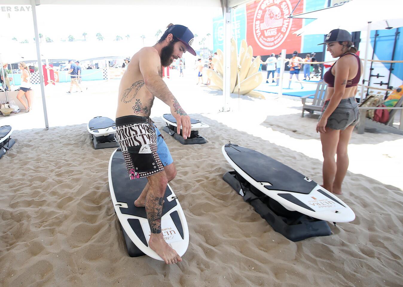 Fabio Taeliferri pretends to hang 10 as he participates in the "Surfer Says" workout program on moveable boards with friend Lila Rodriquez on Tuesday at the Vans U.S. Open of Surfing in Huntington Beach.
