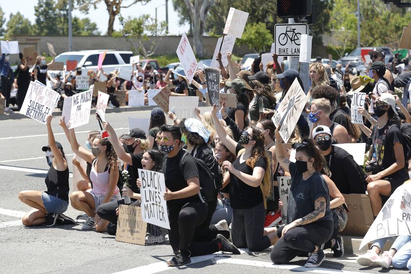Protesters take a knee at the entrance to Fashion Island during a Black Lives Matter protest which began at MacArthur Boulevard and East Coast Highway in Newport Beach on Wednesday.