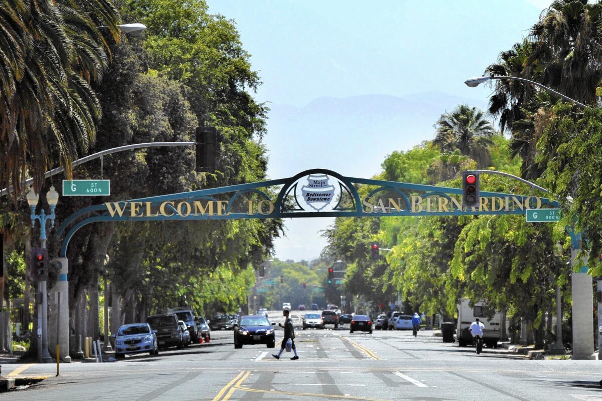 A person walks through an intersection with a "Welcome to San Bernardino" sign spanning overhead.