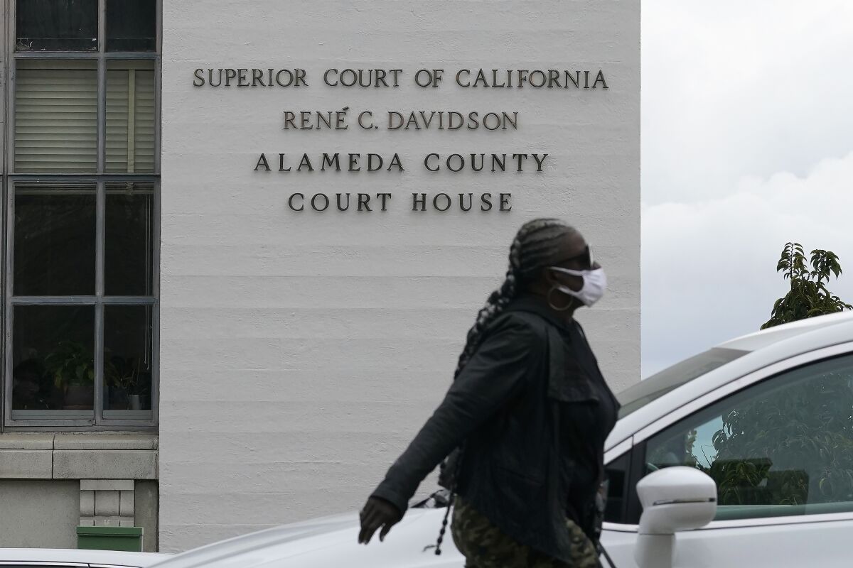 FILE - In this March 9, 2021, file photo, a pedestrian wears a face mask while walking across the street from the Alameda County Court House during the coronavirus outbreak in Oakland, Calif. California's Alameda County said Thursday, June 2, 2022 it will reinstate an indoor mask policy in an effort to ease as coronavirus cases surge in the nation's most populous state. (AP Photo/Jeff Chiu, File)