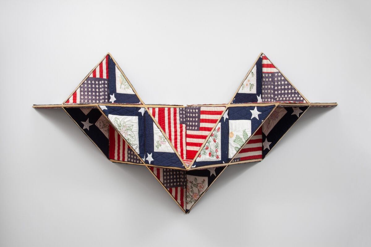 An angular, three-dimensional wall sculpture is made from scraps of quilts and pieces of American flags.