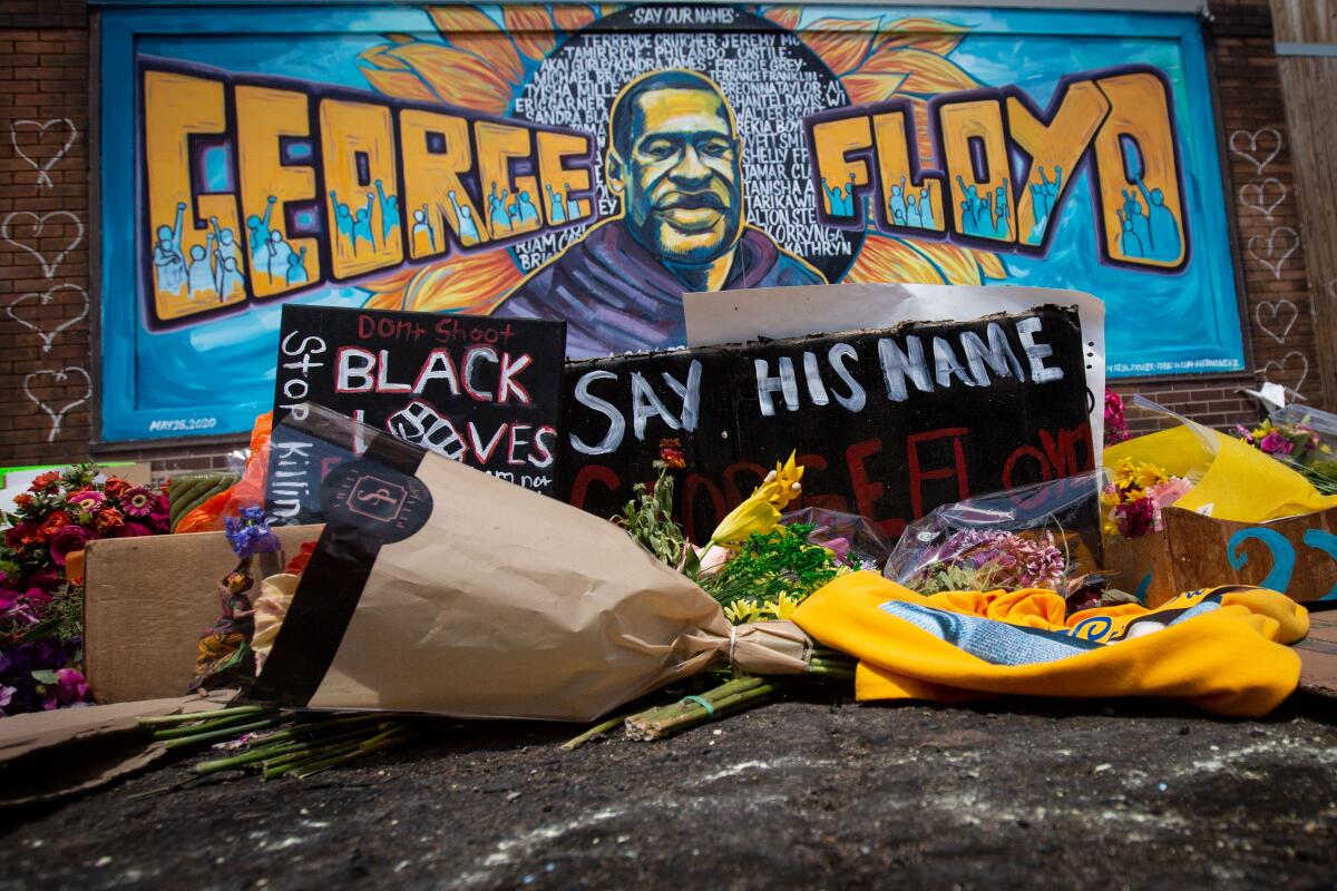 A makeshift memorial is set up in front of a blue and orange George Floyd mural. 