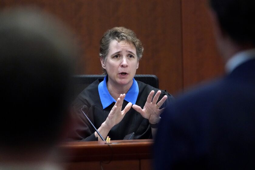 A judge gestures from the bench as she talks to two attorneys in court