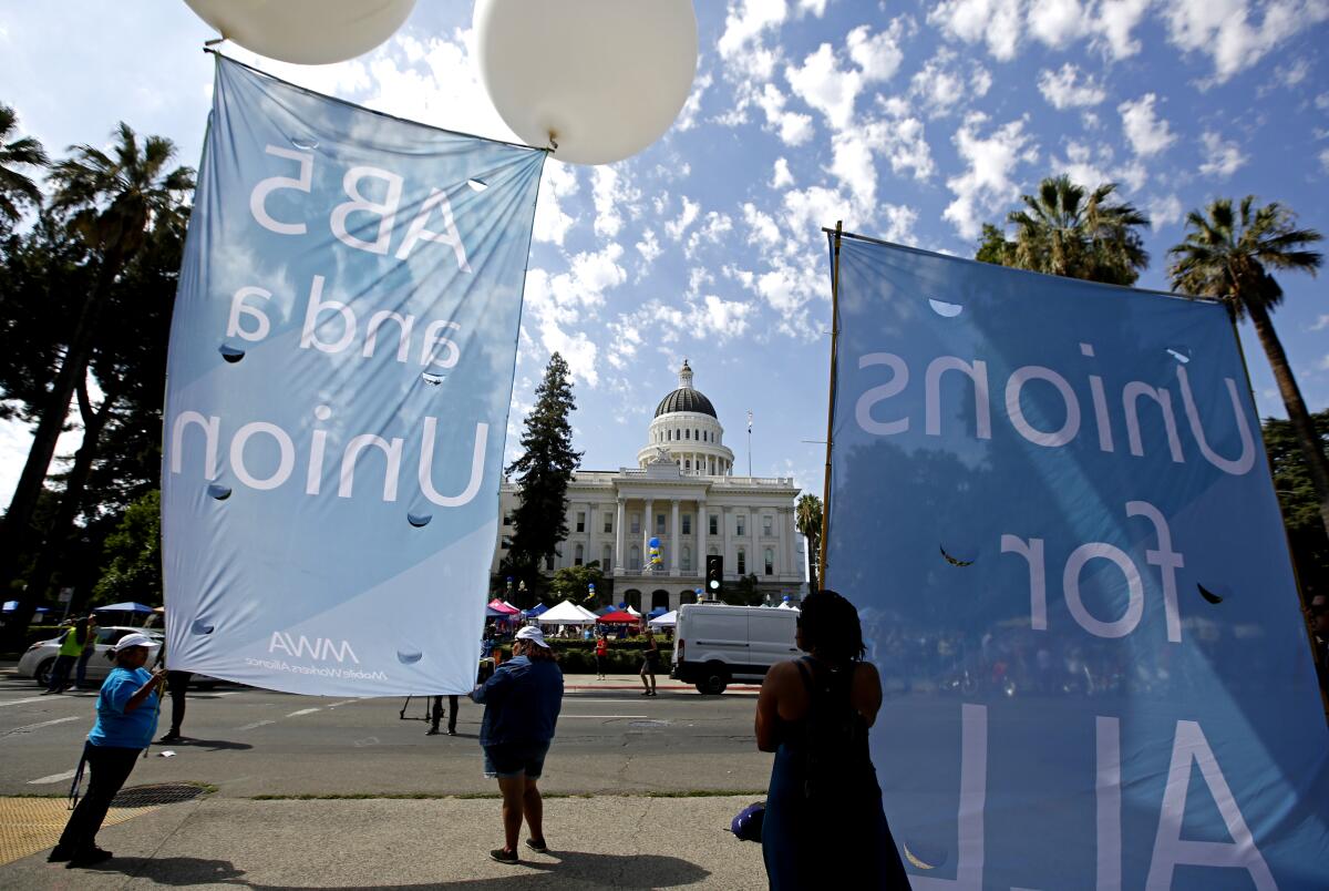 Supporters of a measure to limit when companies can label workers as independent contractors display banners Wednesday in Sacramento.