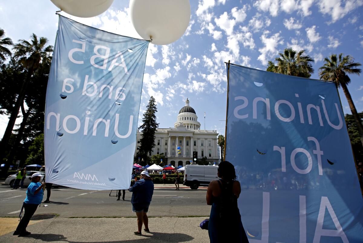 Supporters of a measure to limit when companies can label workers as independent contractors display banners Wednesday in Sacramento.