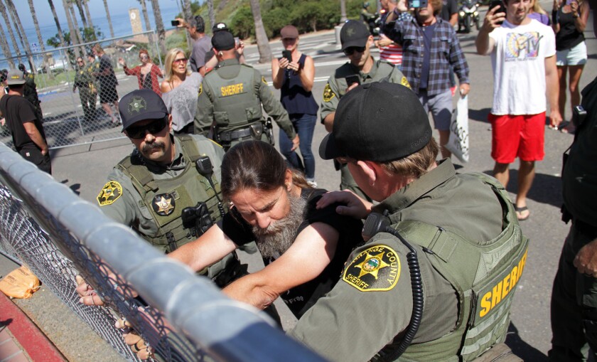 Alan Hostetter clings to a fence at the Pier Bowl parking lot as part of a rally