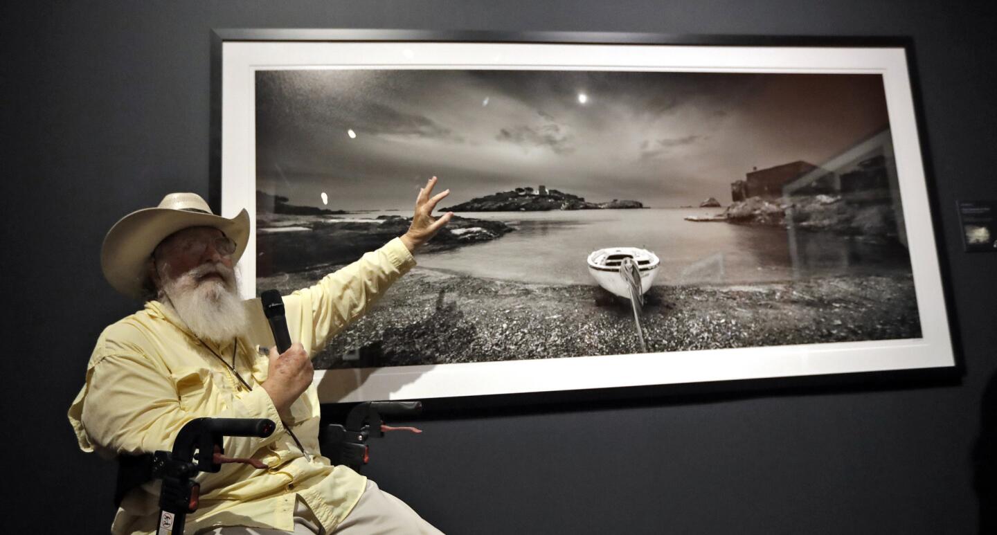 Clyde Butcher gestures as he gives a description of one of his photographs during the opening of his "Clyde Butcher, Visions of Dali's Spain" exhibit, at the Salvador Dali Museum Friday, June 15, 2018, in St. Petersburg, Fla. The new exhibit features photographs of the places in Spain where Dali lived, shot by Butcher, a photographer renowned for his pictures of the Florida Everglades. (AP Photo/Chris O'Meara)