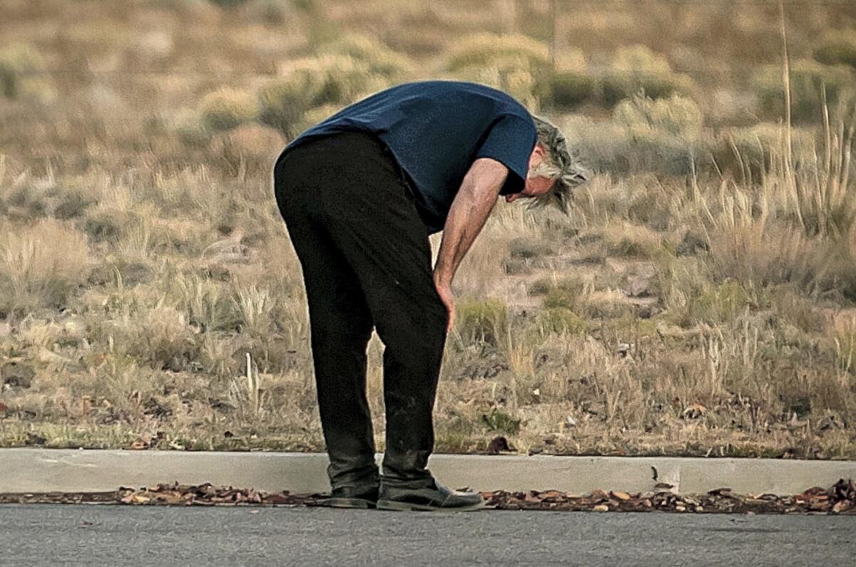 A man dressed in black stands bent over, hands on knees, facing away from the camera.
