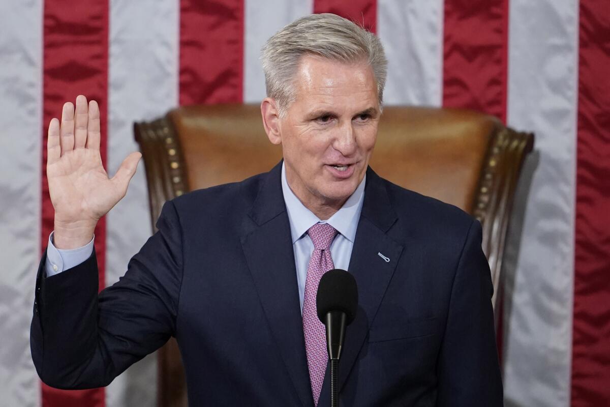 Rep. Kevin McCarthy stands in front of a U.S. flag and raises his hand.