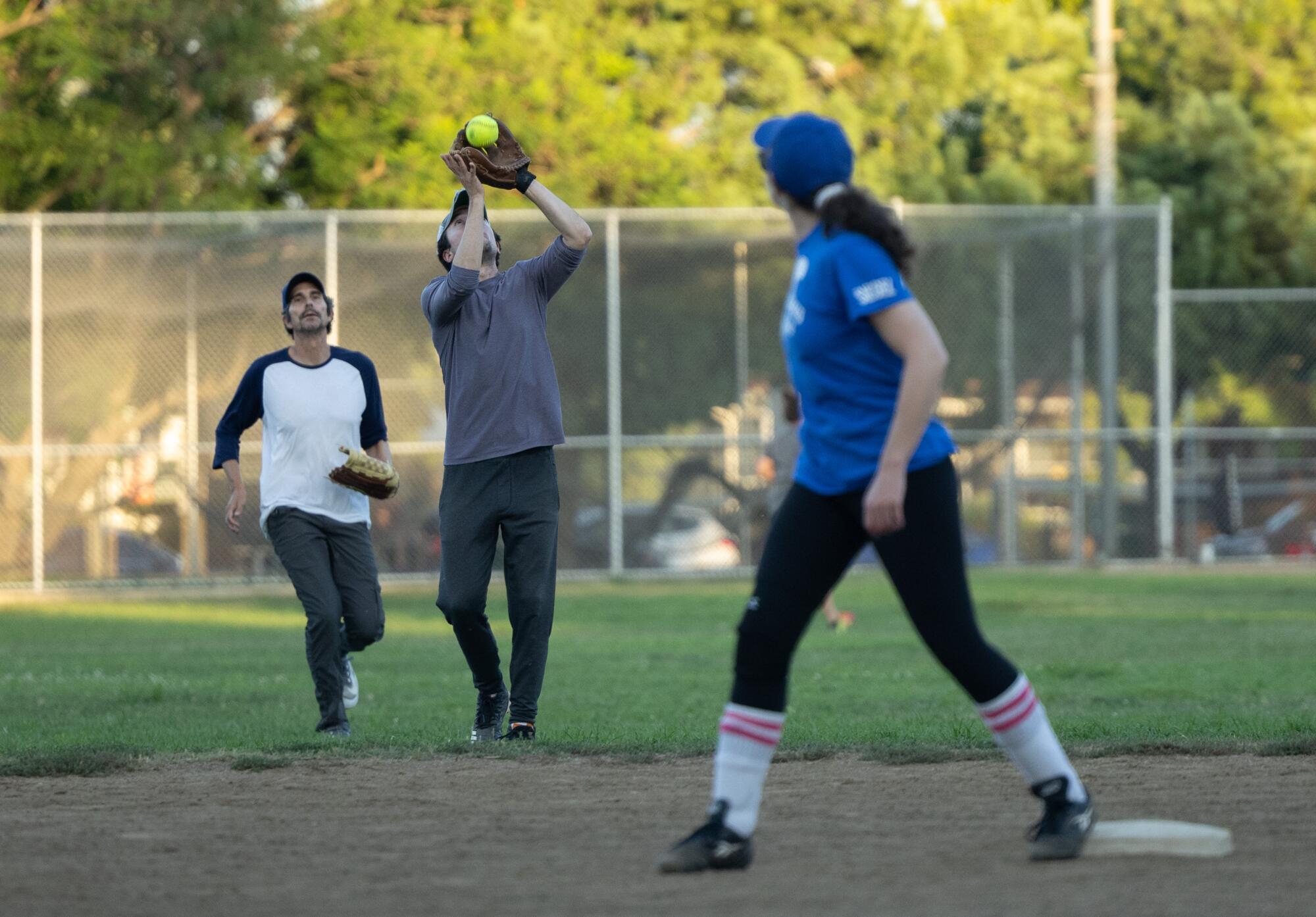 A person catches a softball with a mitt as two people watch.