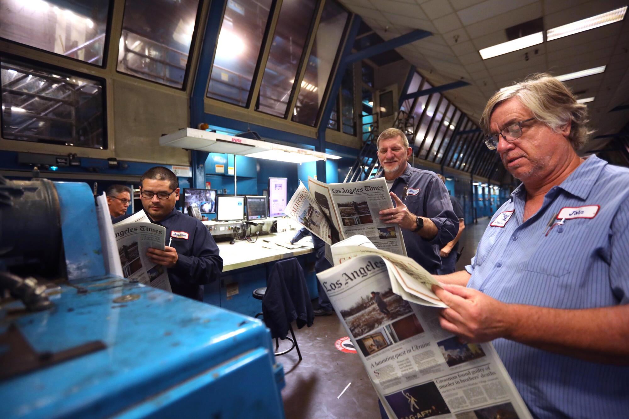 Three men review newspapers at the Los Angeles Times Olympic Printing Plant.