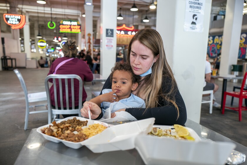 A woman and a baby eat from takeout containers in a food hall