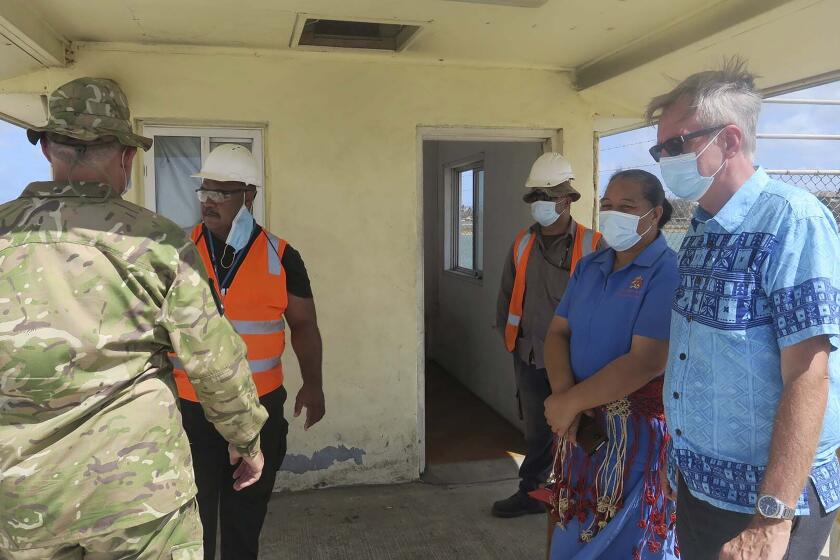 In this photo released by the New Zealand High Commission, Peter Lund, right, New Zealand’s acting high commissioner to Tonga, stands with military personnel at a wharf in Nuku'alofa, Tonga Friday, Jan. 21, 2022, after a New Zealand ship arrived with water and other much-needed aid supplies. (New Zealand High Commission via AP)