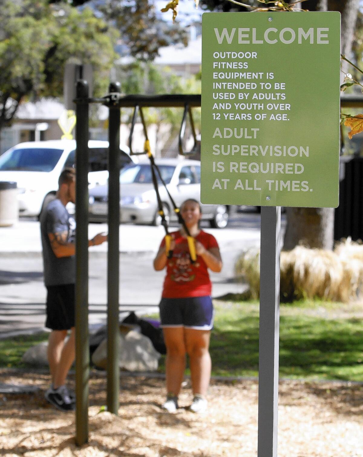 Rachel Barker, 19, of Tujunga, with the help of personal trainer Tony Snyder, left, works out in the recently built area designated only for those age 12 and older, at Maple Park in Glendale on Thursday, Sept. 4, 2014.