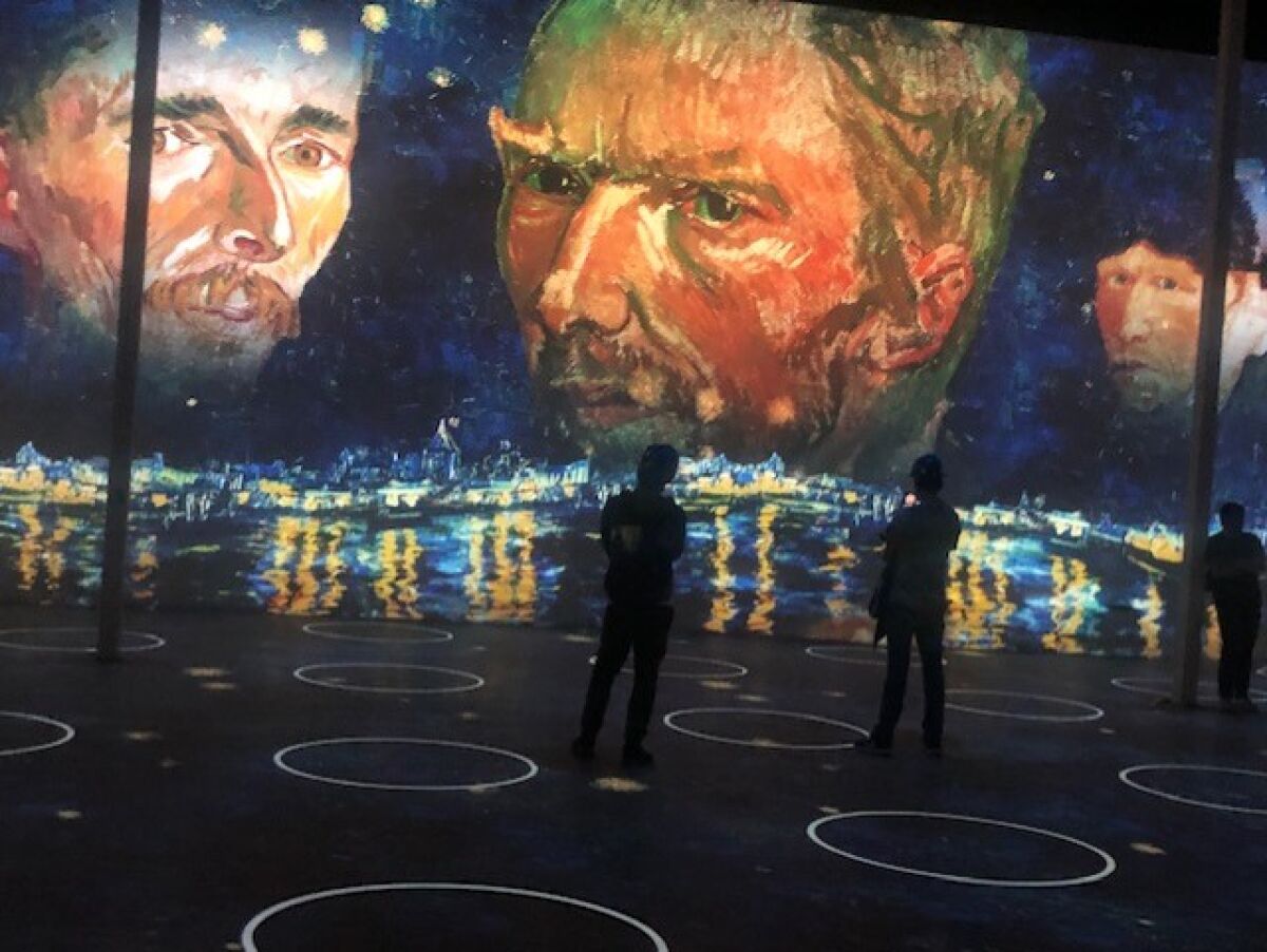 People stand in a darkened room with projections of Vincent Van Gogh on the wall.