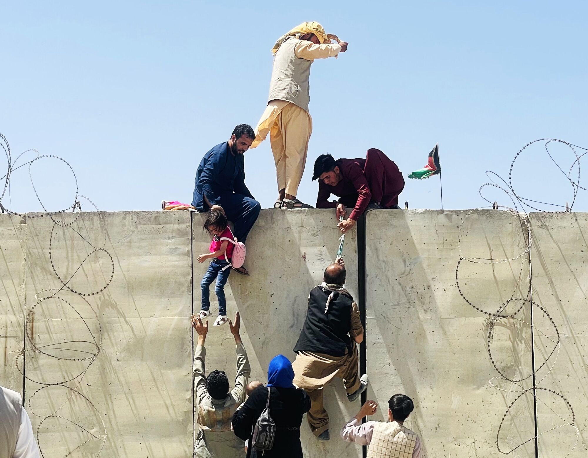 Afghans climb over a tall barrier