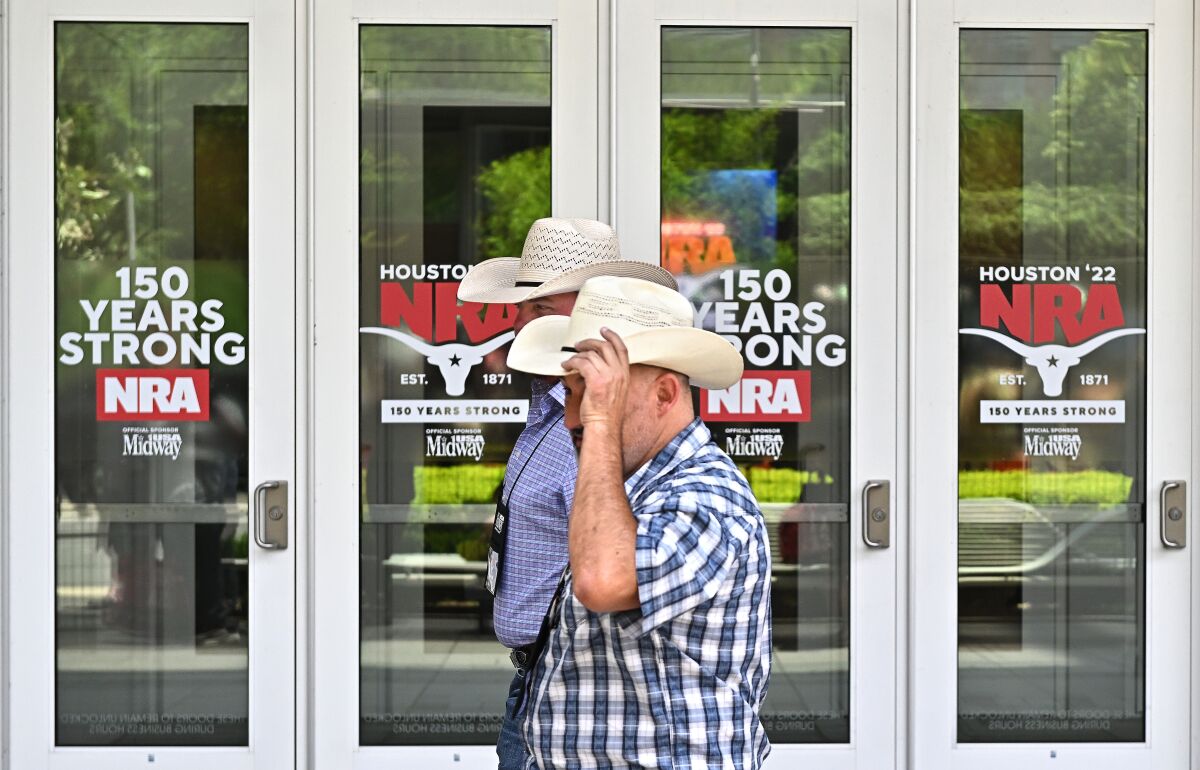 Two men in cowboy hats walking past signs reading "Houston '22 NRA" and "150 years strong" at a building's entrance.