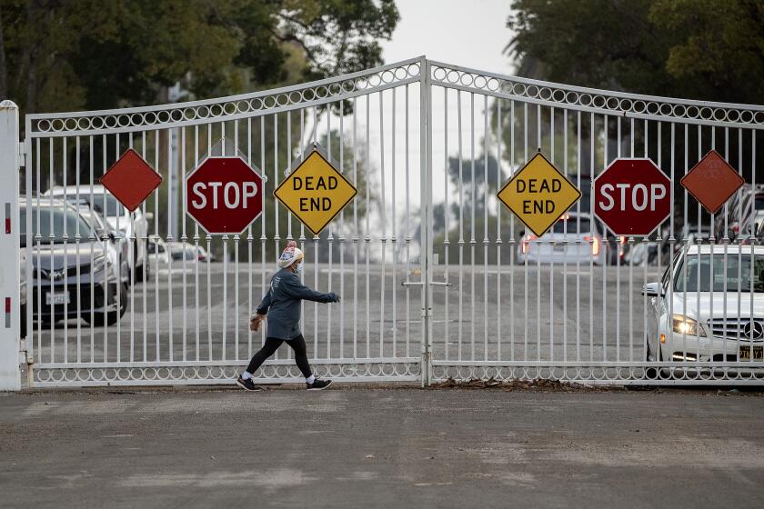 LOS ANGELES, CA-JANUARY 31,2024:A pedestrian walks along Gramercy Place in Los Angeles inside the "Pico Gates," that prevent people or cars from entering north of Pico Blvd. There is movement for and against opening the "Pico Gates," a set of gates that were installed around the Country Club Park neighborhood in an effort to protect them from society ills in the mid 1980's. (Mel Melcon / Los Angeles Times)