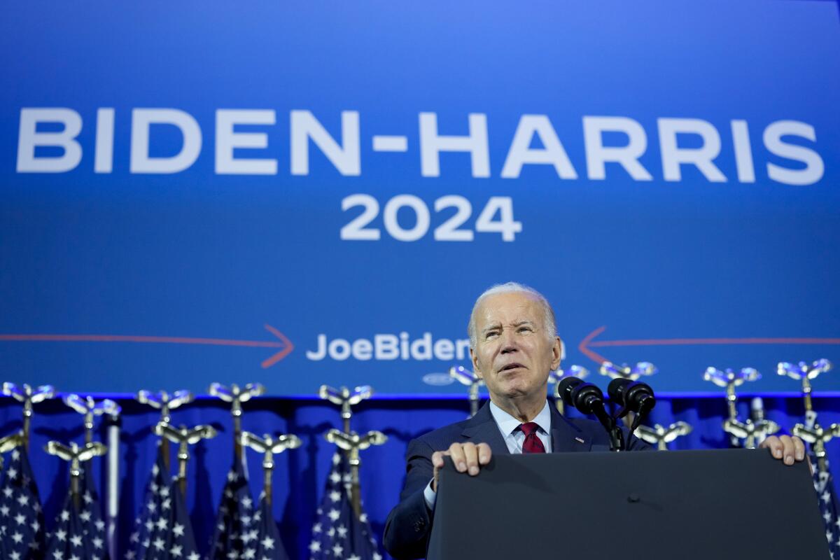 President Biden speaks in front of a blue background with the words "Biden-Harris 2024." 