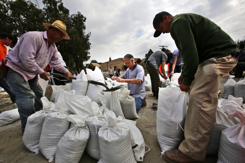 Alvaro Sanchez, left, Jack Watson, center and Salvador Segura fill sand bags at a Glendora city yard. Glendora residents living in and around the area of the Colby fire collected sand bags to protect their residences from the possibility of flash flooding and mud and debris flows caused by expected rains.