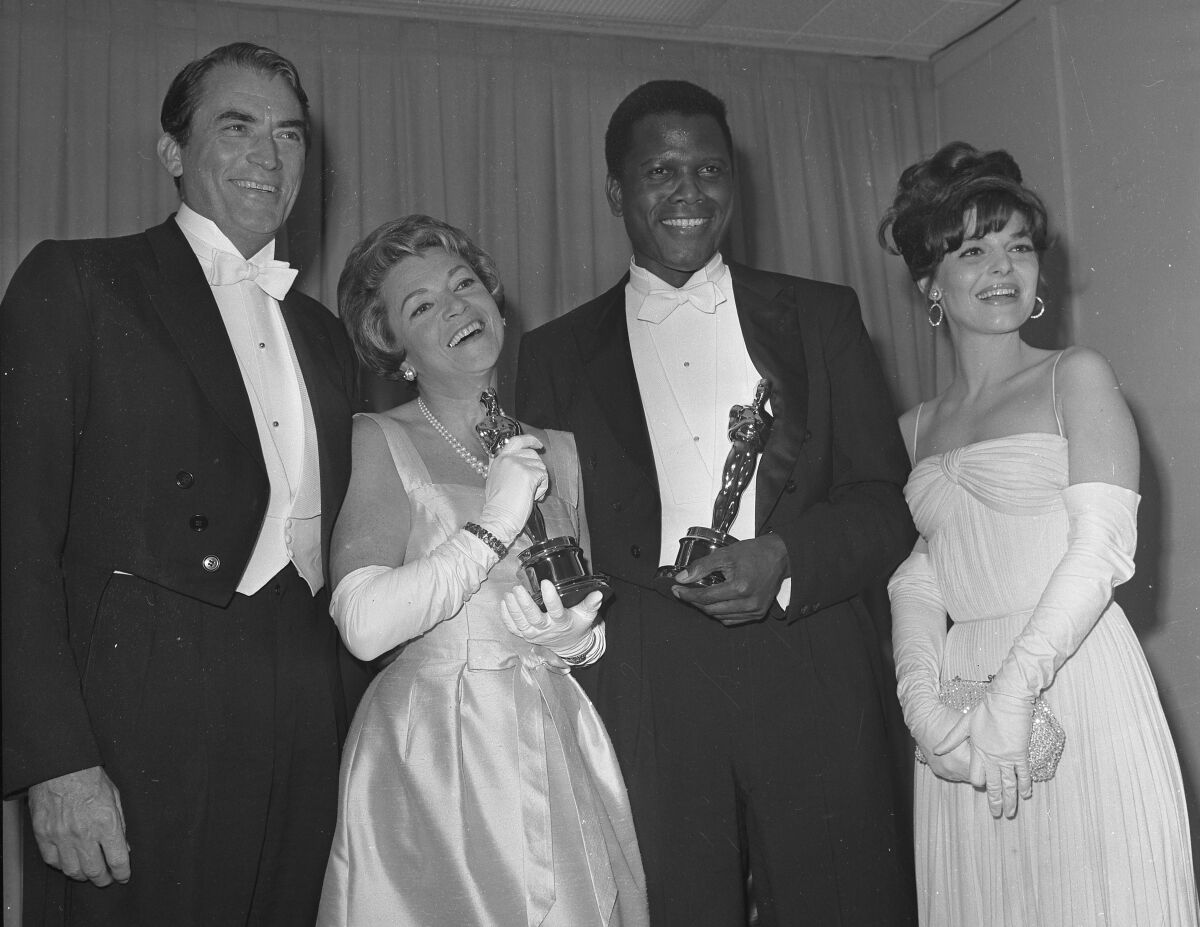 A man and a woman each hold Oscars while posing with two other people