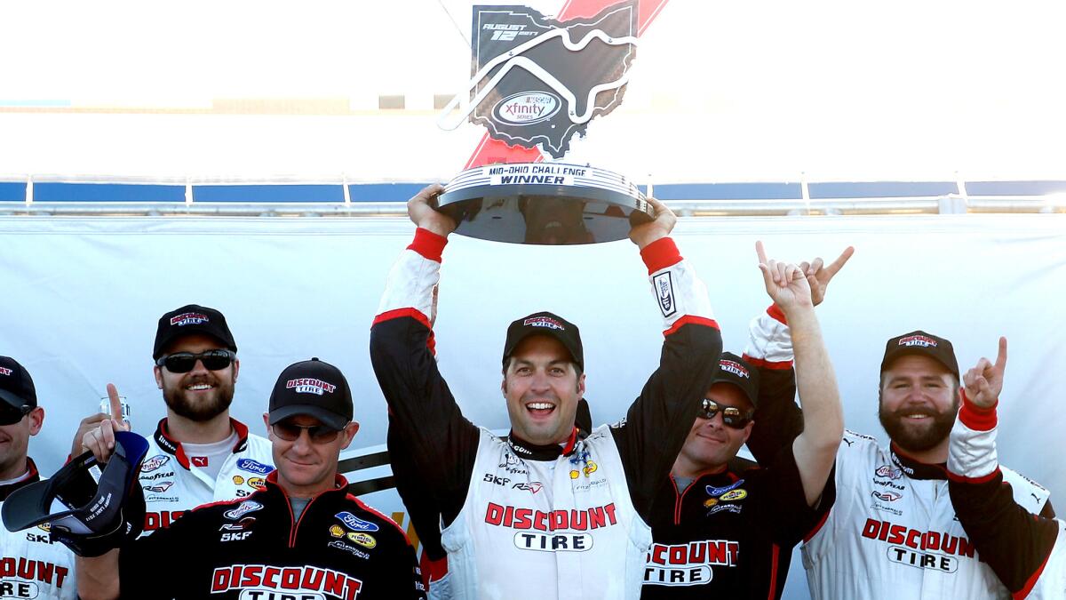 NASCAR driver Sam Hornish Jr. hold aloft the winner's trophy as he celebrates in Victory Lane with teammates after the Xfinity Series Mid-Ohio Challenge on Saturday.