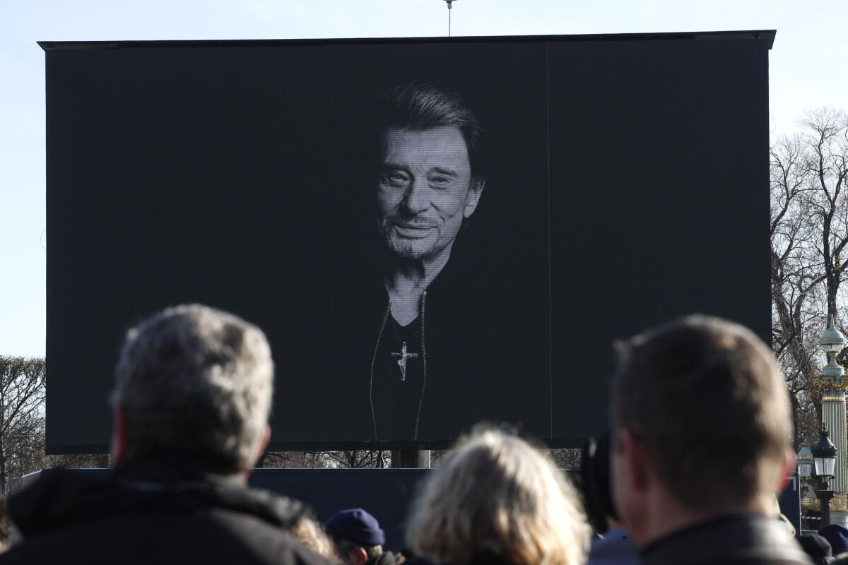 Personas observan el funeral de Johnny Hallyday en una pantalla gigante en París, el sábado 9 de diciembre de 2017. Johnny Hallyday, el más grande rockero francés, recibió un funeral excepcional en los Campos Elíseos, un desfile y un discurso presidencial bajo seguridad estricta.