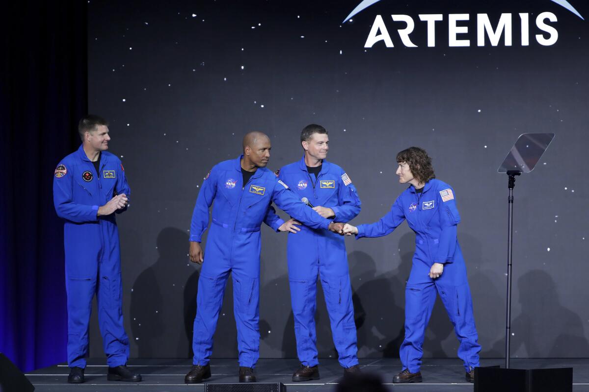 Four people in blue coveralls stand on a stage. Two of them bump fists.