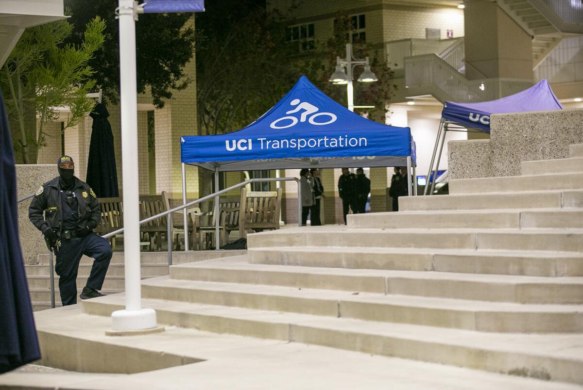 Police officers stand around two canopies set up next to steps at a crime scene on campus