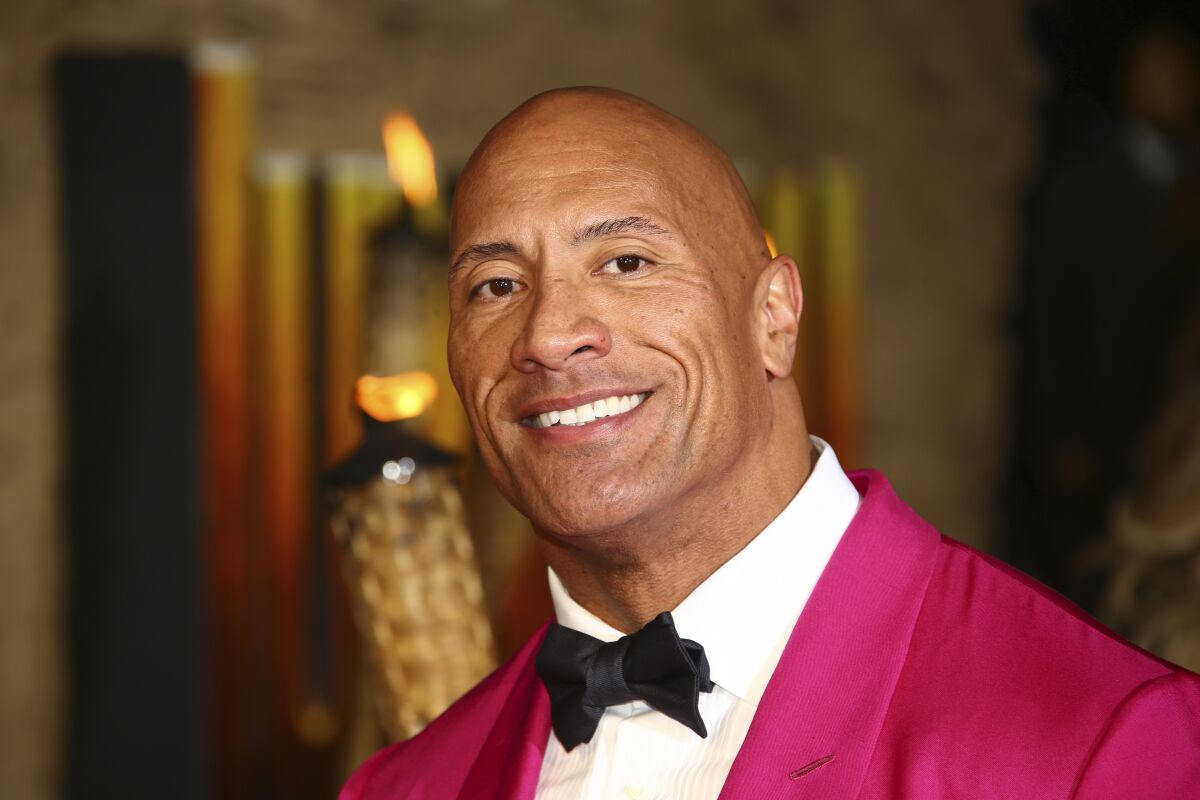 Dwayne Johnson smiling in a pink suit and tie
