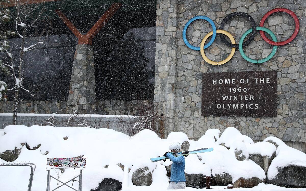 A skier walking past a sign at Palisades Tahoe denoting the ski resort as the site of the 1960 Winter Olympics.