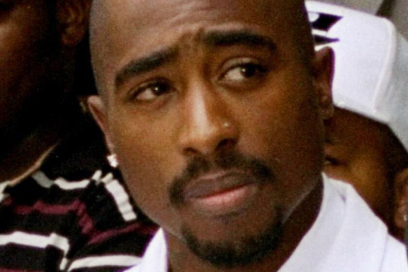 An old photo of Tupac Shakur wearing a white suit and looking to his left.