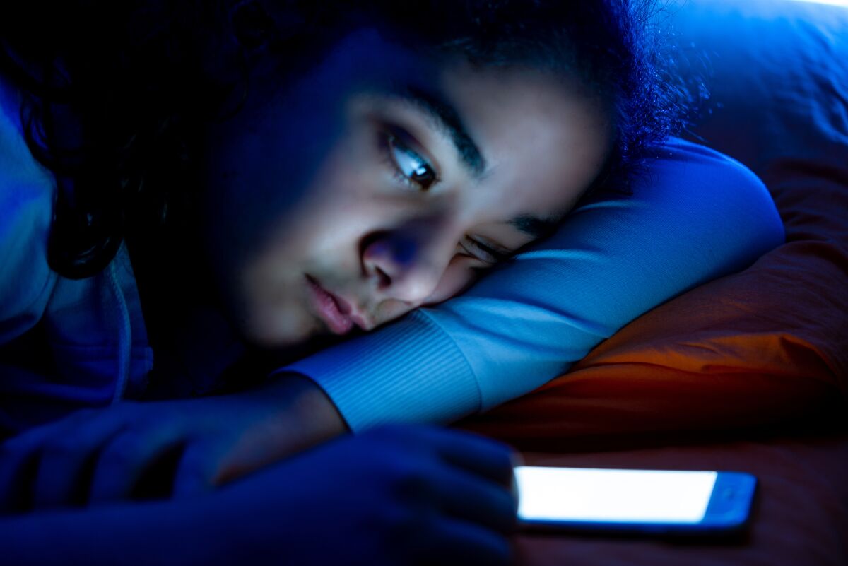 A girl looks at her smartphone while in her dark bedroom.