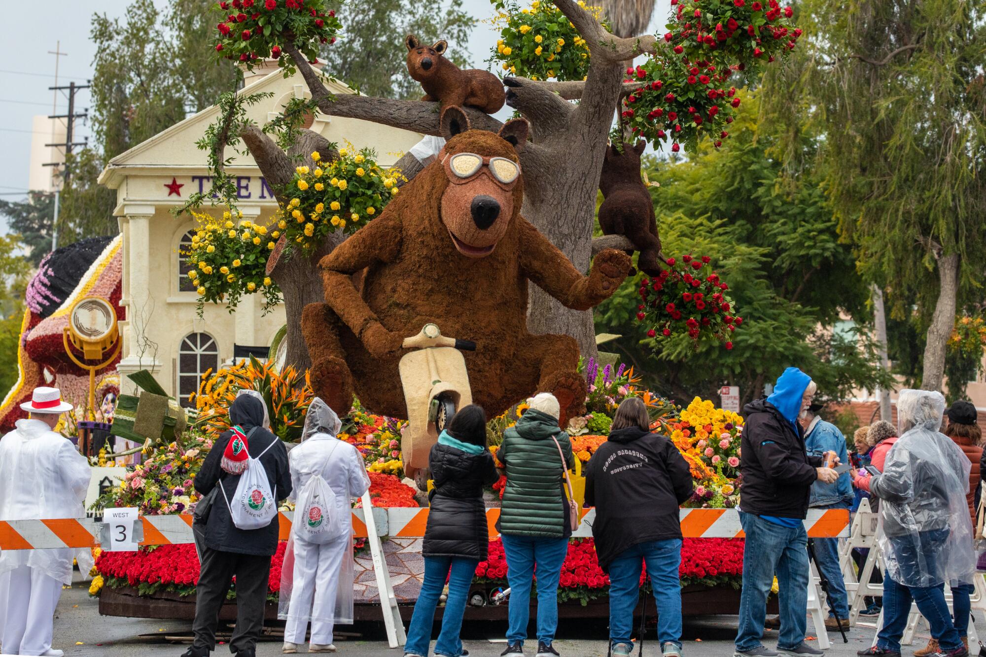 Visitors look at a float with a giant bear figure wearing sunglasses and riding a vespa 