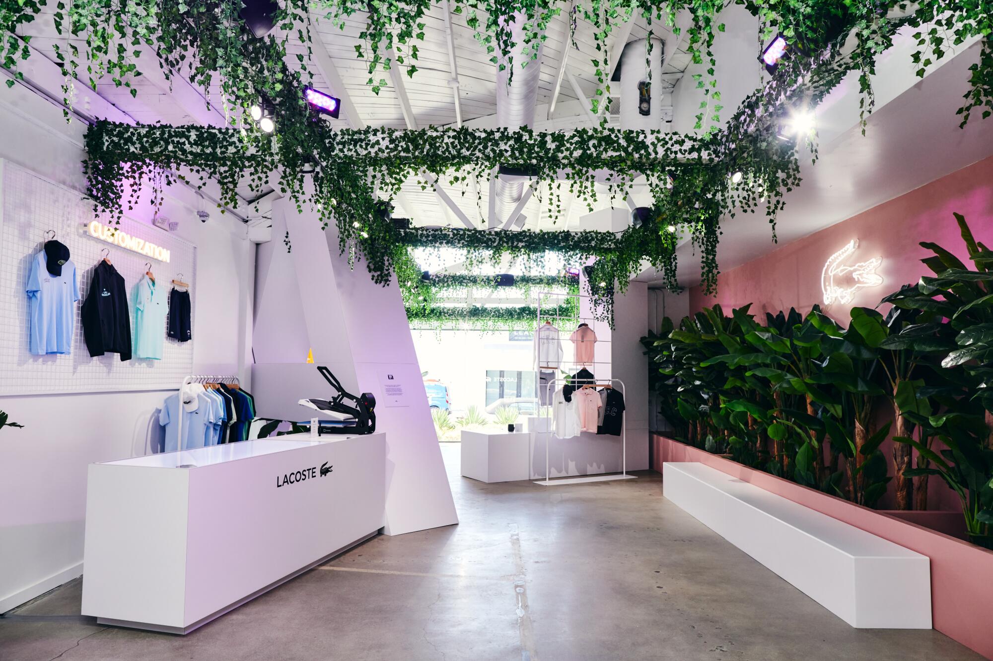 Inside of the Lacoste pop-up shop featuring greenery along the wall and ceiling, a neon alligator sign, and hanging products
