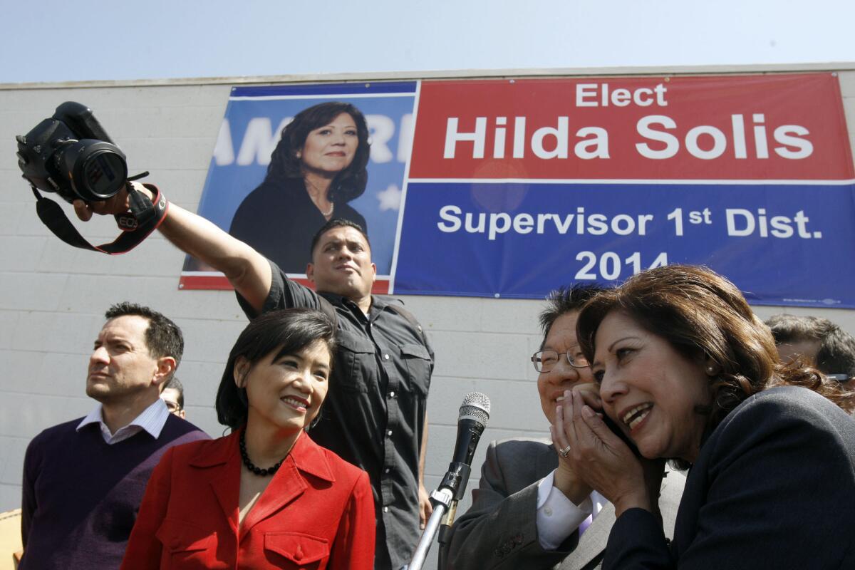 Hilda Solis, right, tries to listen to a cellphone call during a campaign rally on April 5 in El Monte.