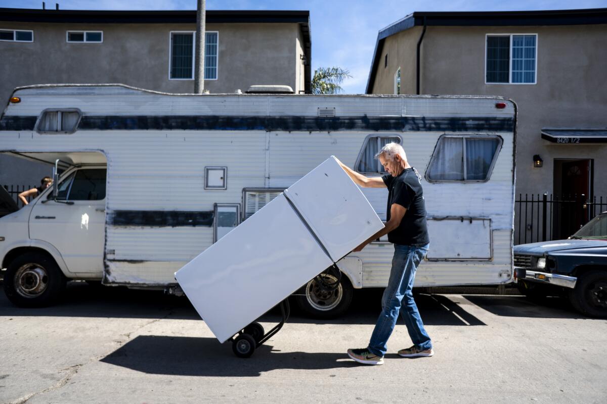 John Betz rolls a refrigerator down Wall street outside two duplex housing units for homeless people. 