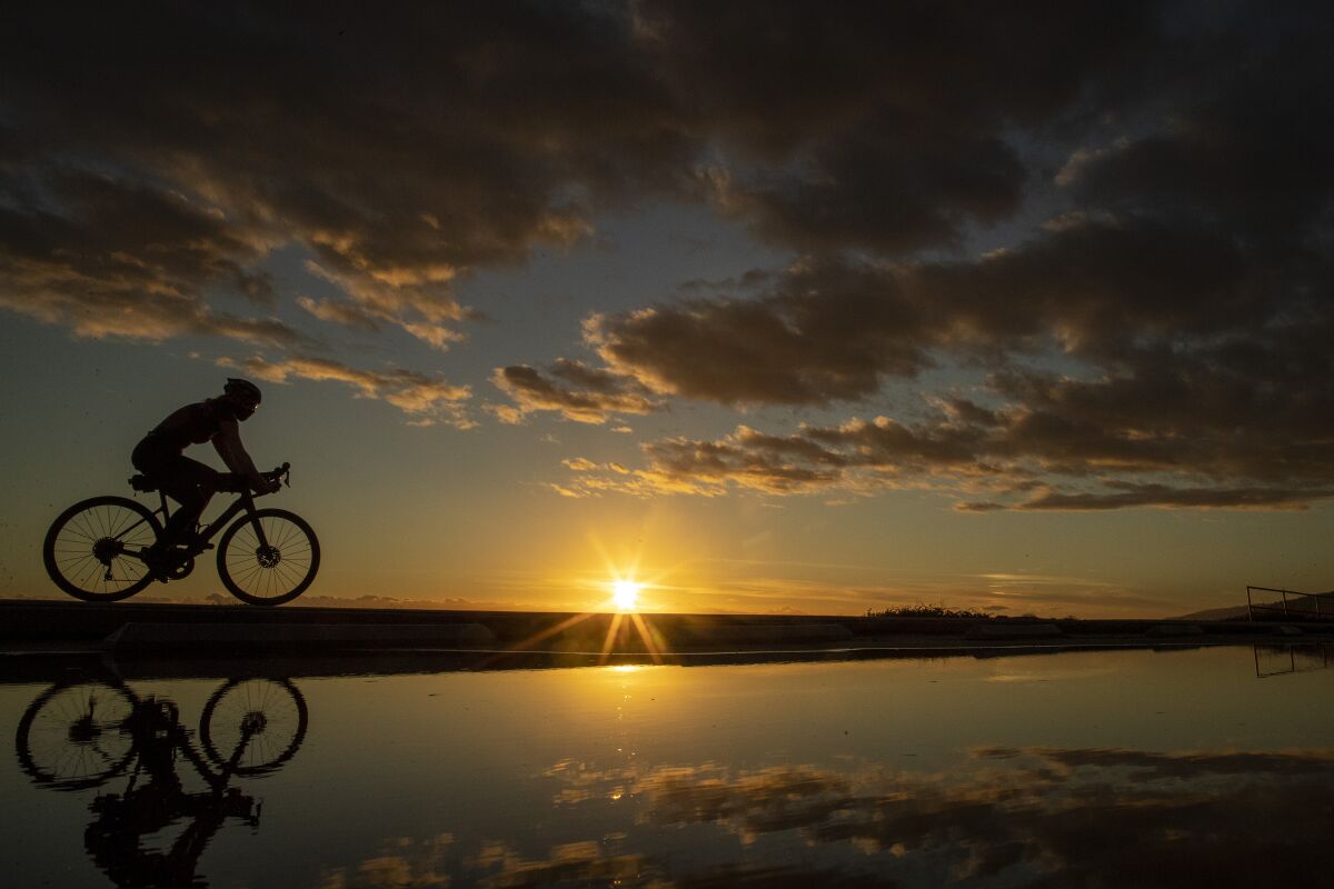 A cyclist is reflected in puddles at sunset.
