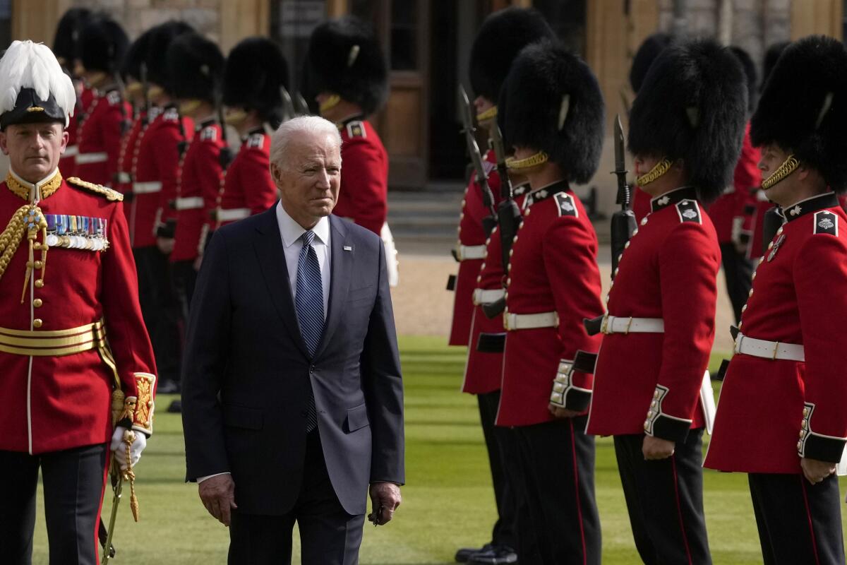 On a green field, Biden walks past a row of men in uniform and bearskins, or tall fur hats.
