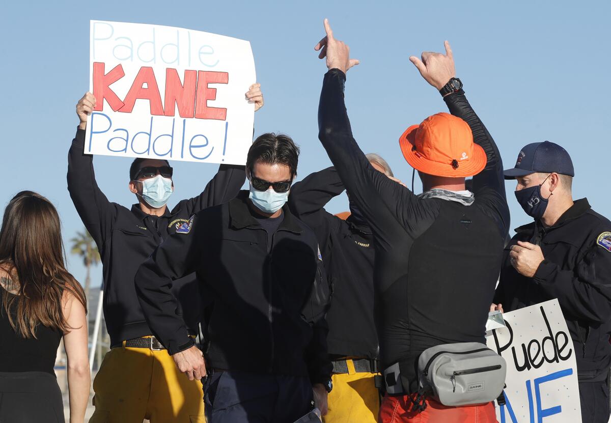 Huntington Beach fire engineer Kane Johnson, in orange hat, arrives to the beach with cheers from his crew.