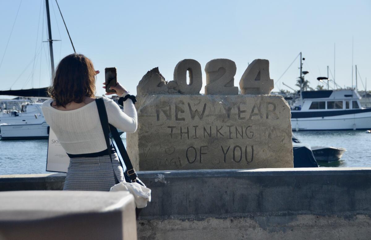 A woman takes a photo of a sand sculpture by Chris Crosson on Balboa Island to welcome the new year. 