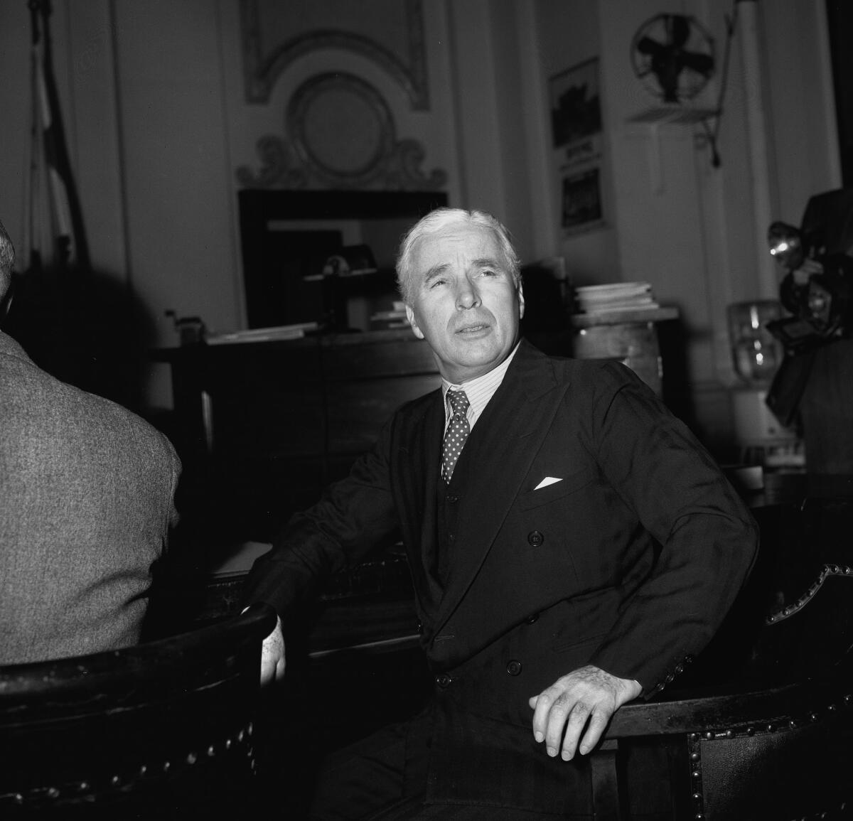 A man with white hair and a suit and tie sits in court.