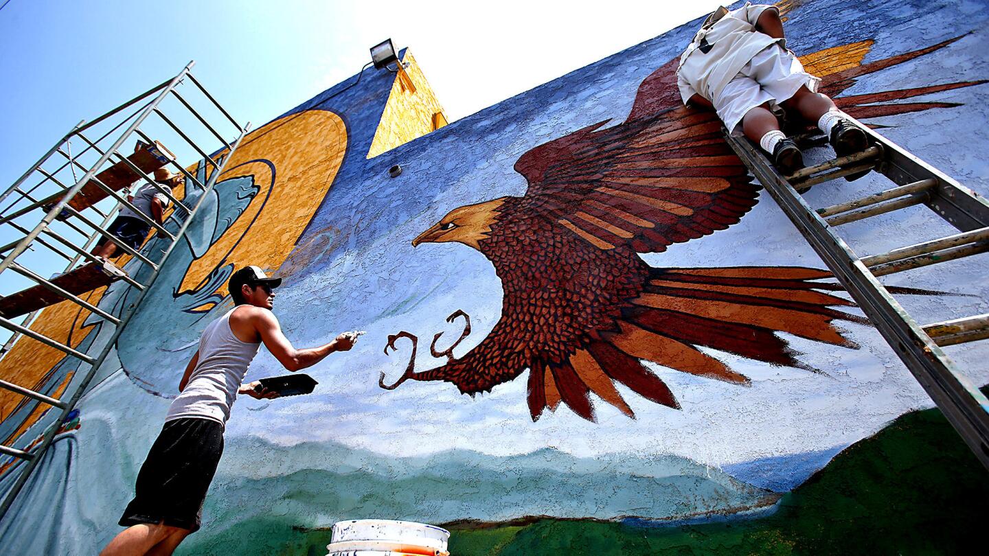 Levi Ponce, center, is assisted by fellow artists as he works on a painting on Mural Mile on Van Nuys Boulevard.