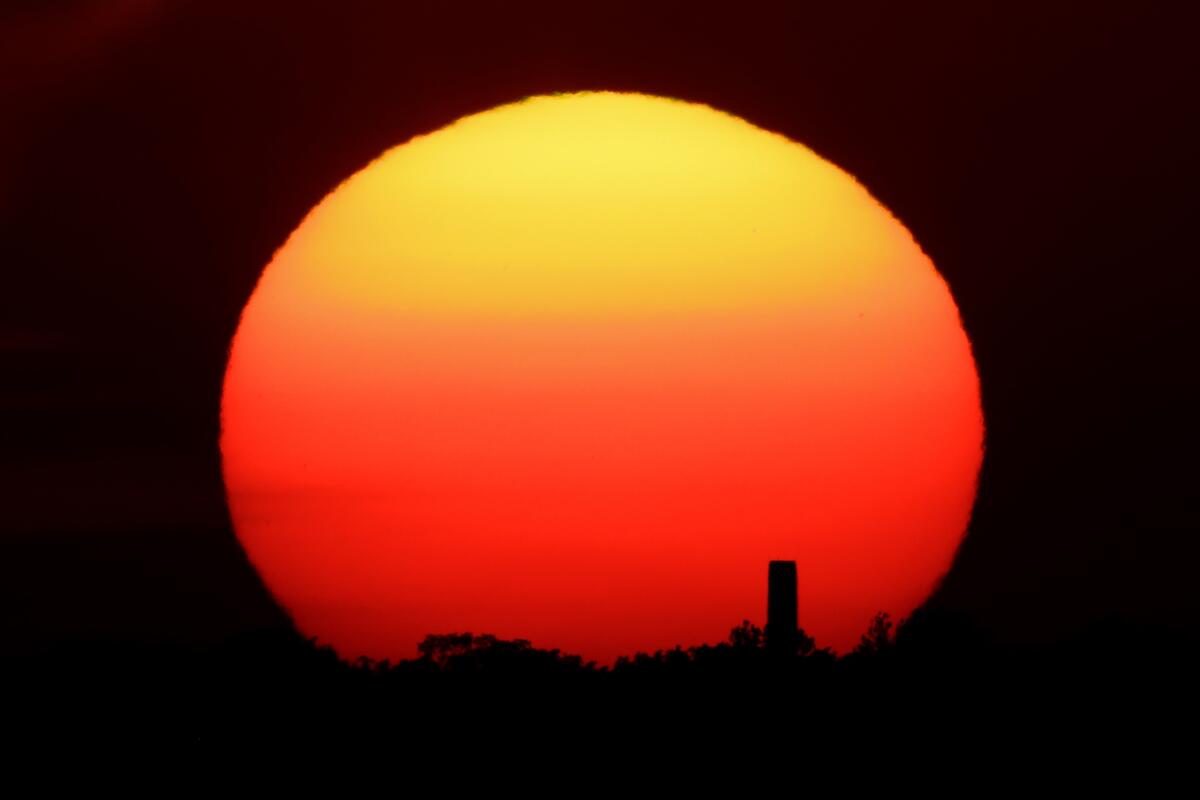 The bright orange sun silhouettes a smokestack