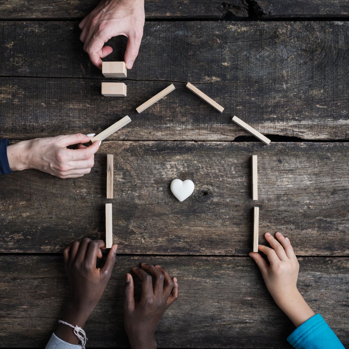 Family of four with kids of caucasian and african american race, building a house of wooden blocks with heart inside it