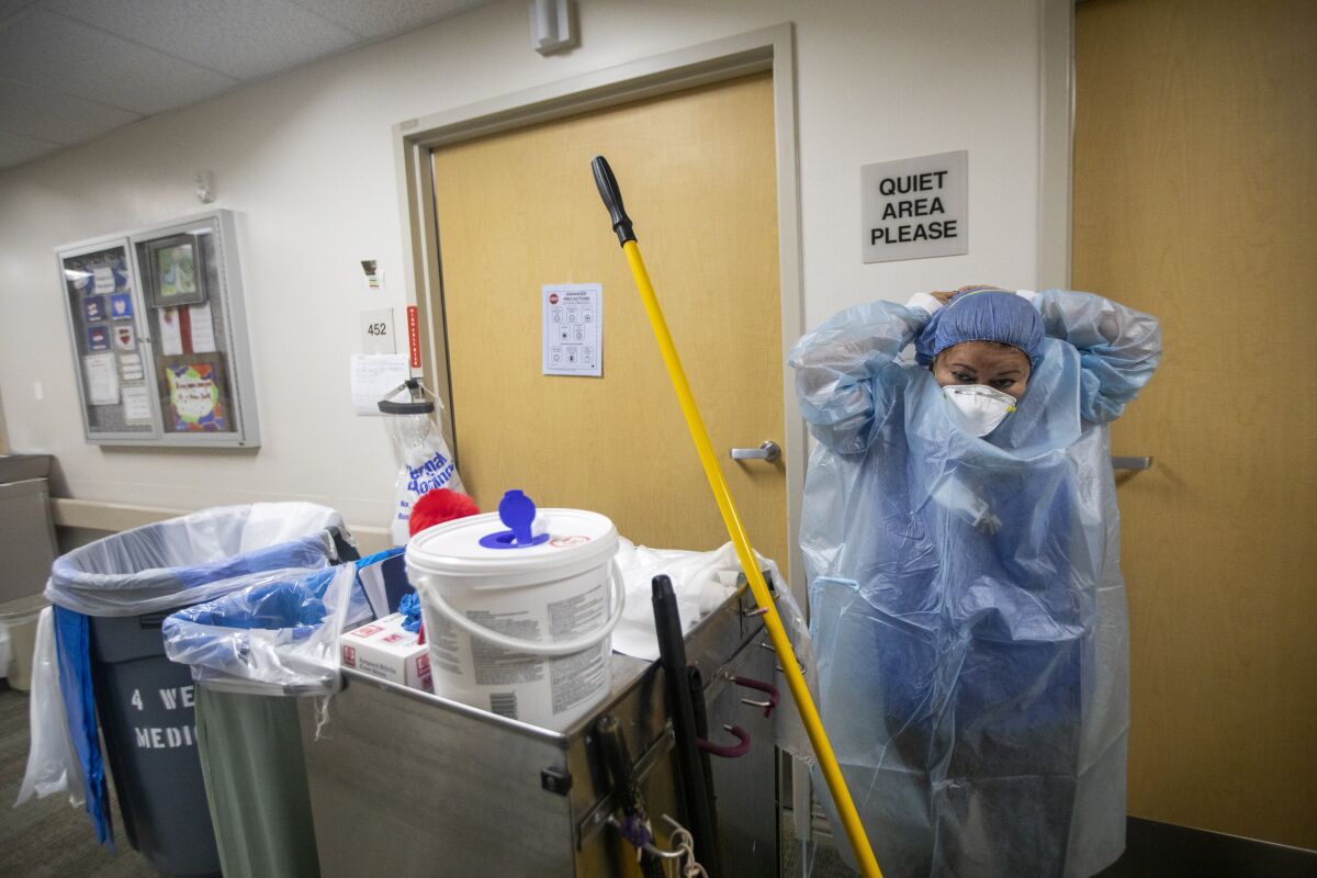 A hospital janitor reaches back to put on her protective equipment outside the COVID-19 unit